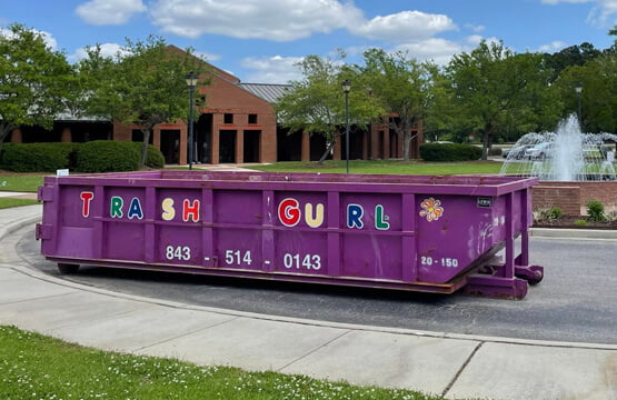 Large brick building with Trash Gurl dumpster by fountain.
